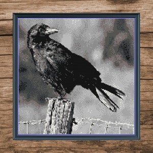 May include: A black crow perched on a wooden post against a blurry, gray background. The crow has its wings spread out and its head turned to the side.