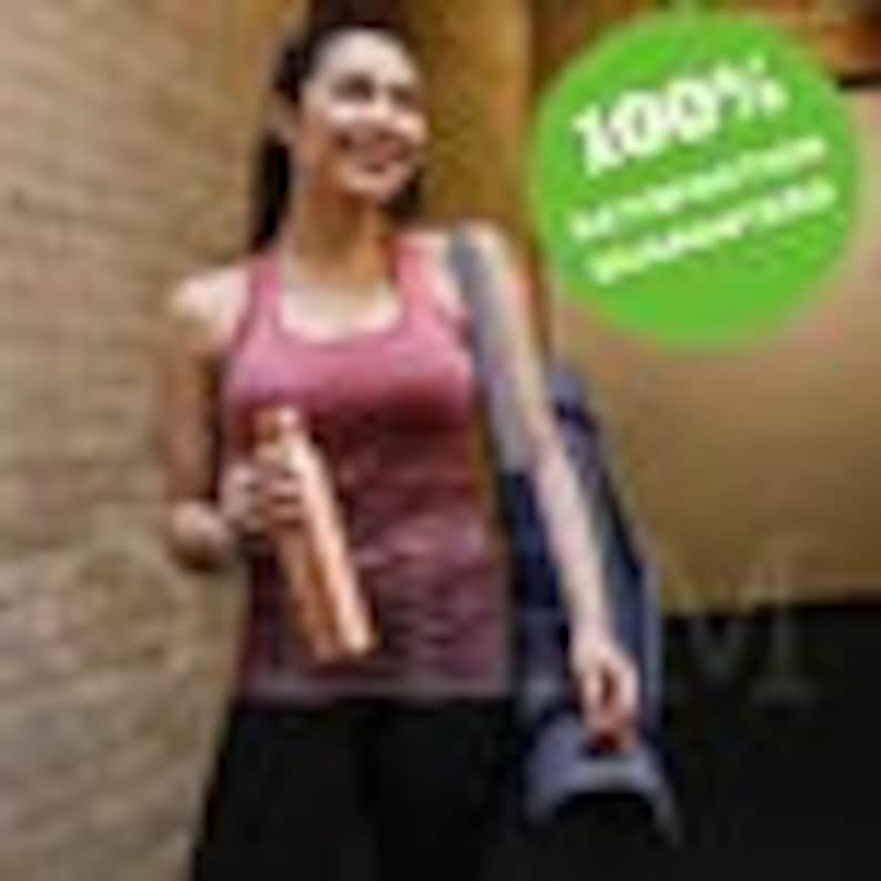 May include: A woman wearing a pink tank top and black trousers is walking down a corridor. She is carrying a reusable water bottle and a black yoga mat. The bottle is made of stainless steel and has a copper finish. The text "100%  sustainable  goodness" is printed on a green circle sticker.