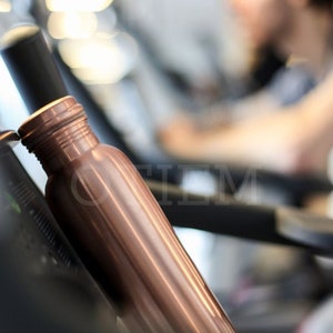 May include: A copper water bottle with a ribbed design. The bottle is sitting on a black surface.