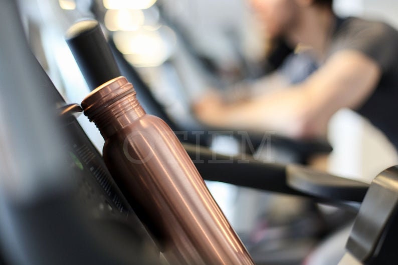 May include: A copper water bottle with a ribbed design. The bottle is sitting on a black surface.