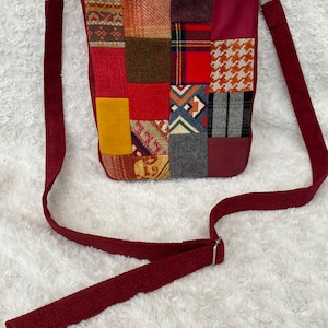 Op de afbeelding: Een bordeauxrode patchwork crossbody tas met een lange verstelbare schouderband. De tas is gemaakt van verschillende stoffen in tinten rood, geel, bruin en grijs.