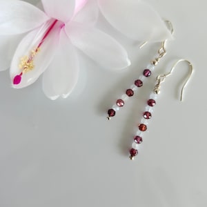 May include: A pair of silver dangle earrings with white and burgundy gemstone beads.