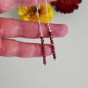 May include: A pair of dangle earrings with a silver chain and a long strand of dark red garnet beads.