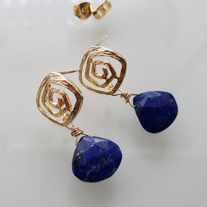 May include: Gold earrings with a geometric design and a blue lapis lazuli stone dangle.