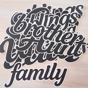 May include: Black and white die-cut words spelling out "siblings brother aunt family" in a cursive font. The words are stacked on top of each other, with a white border around each word.