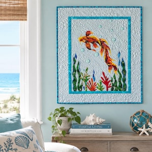 May include: A rectangular fabric wall hanging featuring a central koi fish in shades of orange and yellow, surrounded by green and red aquatic plants and light blue bubbles, all set against a light blue background with a textured quilted pattern.