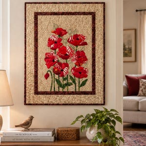 Peut inclure: Une tenture murale rectangulaire en tissu présentant une application centrale de coquelicots rouge vif avec des tiges et des feuilles vertes. Le motif floral est sur un fond beige texturé, encadré par une bordure marron foncé mouchetée.
