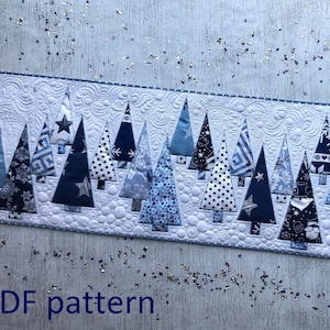 Puede incluir: Un camino de mesa acolchado con una fila de árboles de Navidad estilizados en varios tonos de azul y blanco. Los árboles están hechos de telas estampadas, incluyendo lunares y estrellas. El texto "PDF pattern" es visible.