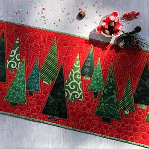 Może przedstawiać: Świąteczny, czerwony, pikowany bieżnik na stół z powtarzającym się wzorem zielonych choinek o różnych wzorach. Drzewa są umieszczone na czerwonym tle z wirującym wzorem. Bieżnik ma złoty brzeg.