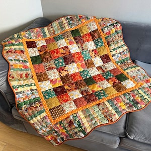 Könnte beinhalten: Ein Patchwork-Quilt mit gewelltem Rand, mit Stoffen in Grün, Orange, Braun und Gelb. Der Quilt hat ein zentrales quadratisches Muster mit einem orangefarbenen Rand. Ungefähre Größe: 150 cm x 150 cm.