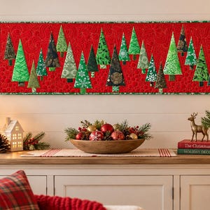 Könnte beinhalten: Ein rechteckiger, gesteppter Wandbehang mit einem leuchtend roten Hintergrund und einem sich wiederholenden Muster aus verschiedenen grünen und dunkel gehaltenen Stoff-Weihnachtsbäumen. Das Stück hat einen grünen Rand und feine Steppnähte.