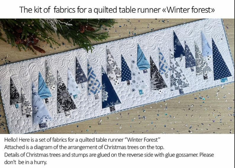 May include: A fabric kit for a quilted table runner titled Winter Forest, featuring a white background with quilted swirl patterns and various blue, navy, and white patterned fabric Christmas tree shapes arranged in a row across the top.