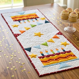 Puede incluir: Un camino de mesa acolchado rectangular con fondo blanco y un tema de cumpleaños repetitivo. El diseño incluye dos pasteles coloridos sobre soportes, estrellas de tela amarilla y banderines triangulares multicolores.