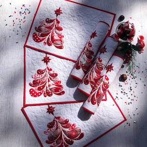 May include: White quilted placemats and rolled table runners with a red Christmas tree design. The tree features red and white patterned fabric with a star on top. The placemats have a red border. Festive holiday decor.