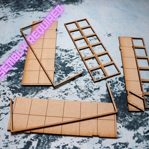 Puede incluir: Un conjunto de piezas de madera sin terminar para construir un modelo. Las piezas son marrones y tienen un patr&oacute;n de cuadr&iacute;cula. El texto "SOME ASSEMBLY REQUIRED" es visible en rosa.