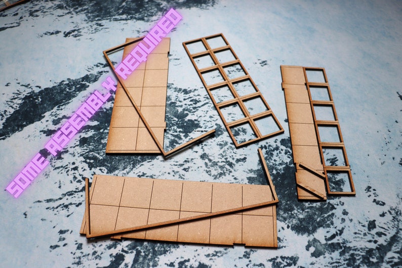 Puede incluir: Un conjunto de piezas de madera sin terminar para construir un modelo. Las piezas son marrones y tienen un patr&oacute;n de cuadr&iacute;cula. El texto "SOME ASSEMBLY REQUIRED" es visible en rosa.