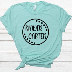 May include: A light blue t-shirt with a black circle design that says "Kindergarten" in a white font.