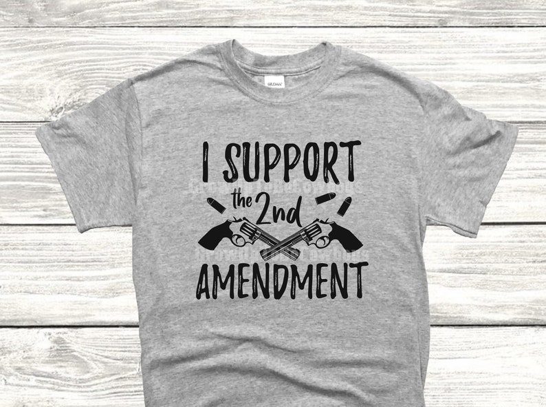 May include: A gray t-shirt with the text "I SUPPORT the 2nd AMENDMENT" printed in black. Two crossed pistols with bullets are depicted above the text.