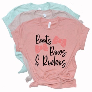 May include: A pink t-shirt with the text "Boots & Bows & Rodeos" in black lettering. Two pink bows are above the text.