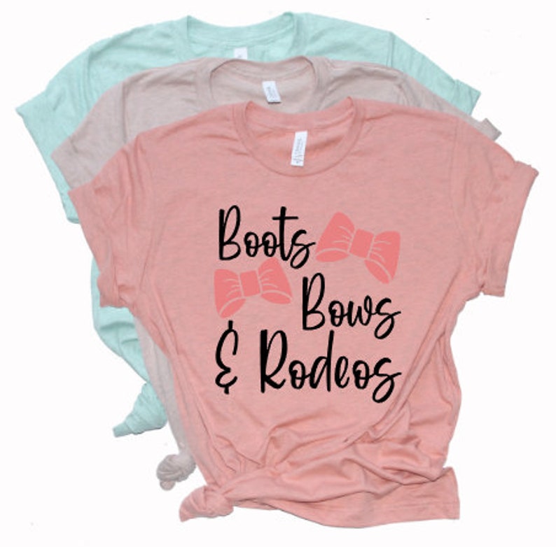 May include: A pink t-shirt with the text "Boots & Bows & Rodeos" in black lettering. Two pink bows are above the text.