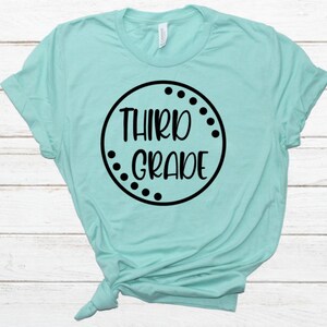 May include: A turquoise t-shirt with a black circle design that says "Third Grade" in a white font.