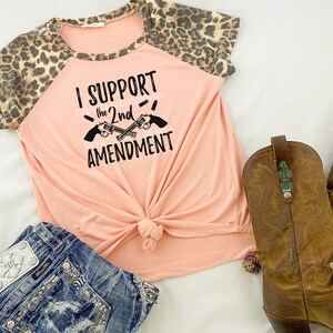 May include: A peach-colored t-shirt with a leopard print on the sleeves. The shirt has a black graphic that says "I Support the 2nd Amendment" with two crossed pistols.