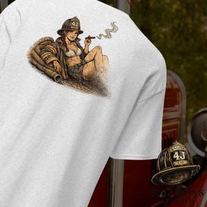 May include: White t-shirt featuring a graphic of a female firefighter in a helmet, jacket, and shorts, smoking a cigar. The image includes a fire hose and the text "4J CO." on the helmet. The shirt also has the text "FODD JOHN'S APPAREL".