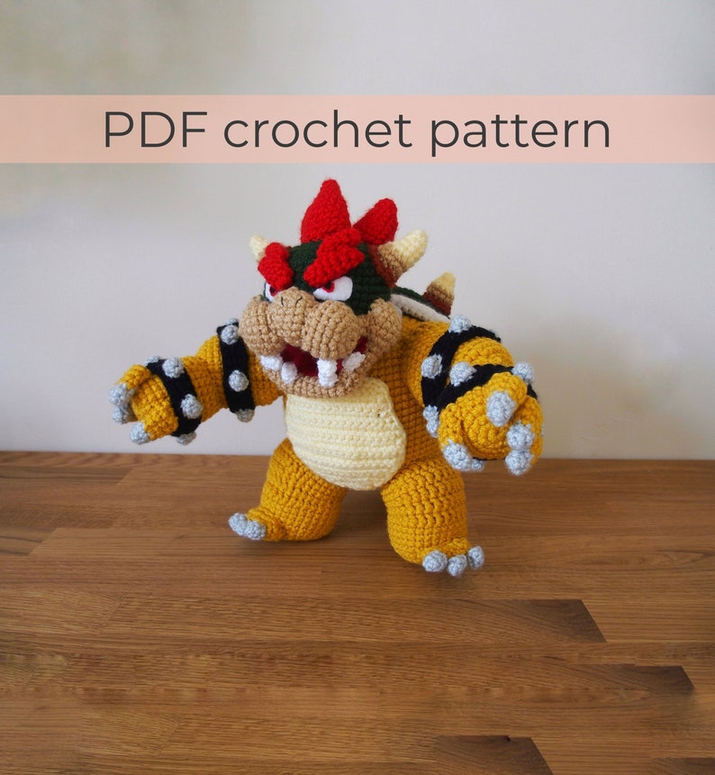 May include: A handmade crochet Bowser doll in yellow, beige, red, and green. The doll has a detailed design with spikes, a shell, and a fierce expression. The text "PDF crochet pattern" is displayed above the doll.