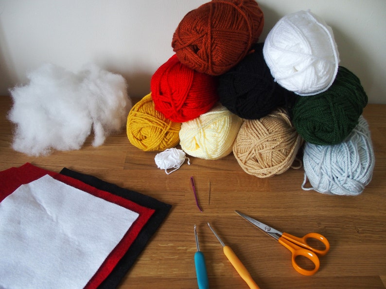 May include: A collection of craft supplies including various colors of yarn, white stuffing, felt squares, crochet hooks, a needle, and scissors. The yarn colors include brown, red, black, yellow, cream, green, and gray.
