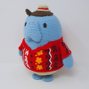 May include: A blue crocheted stuffed animal wearing a brown and beige hat and a red, brown, yellow, and white patterned sweater.