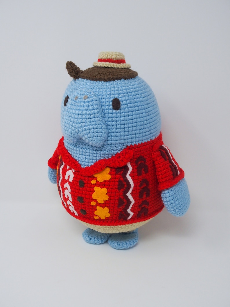 May include: A blue crocheted stuffed animal wearing a brown and beige hat and a red, brown, yellow, and white patterned sweater.