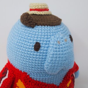 May include: A blue crocheted stuffed animal wearing a red and yellow crocheted jacket and a brown and white crocheted hat.