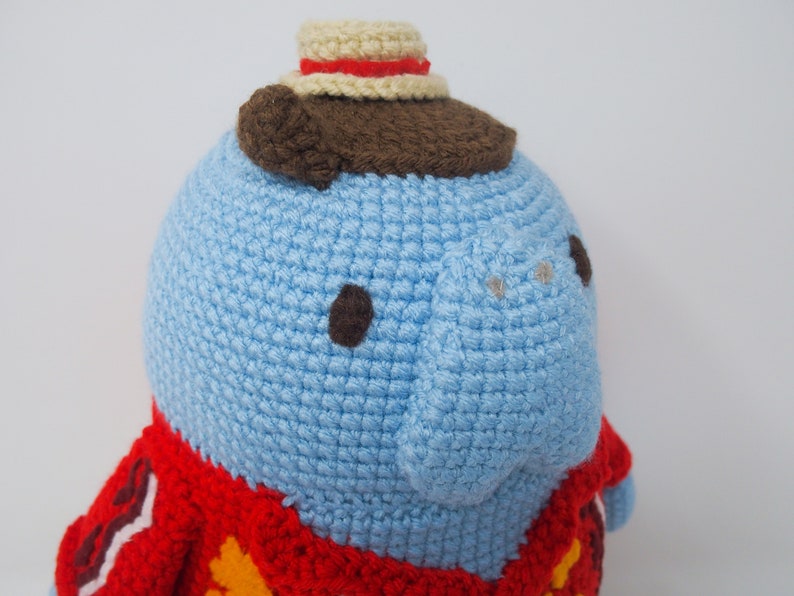 May include: A blue crocheted stuffed animal wearing a red and yellow crocheted jacket and a brown and white crocheted hat.