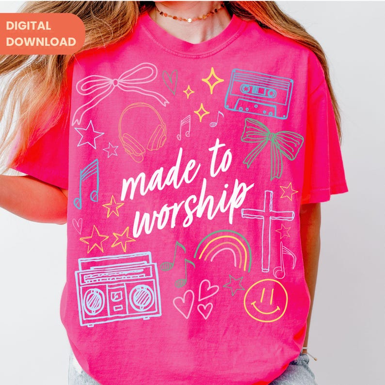 Op de afbeelding: Felroze t-shirt met de tekst "made to worship" in witte letters. Het shirt heeft verschillende doodle-achtige afbeeldingen, waaronder sterren, muzieknoten, een cassettebandje, een koptelefoon en een regenboog.