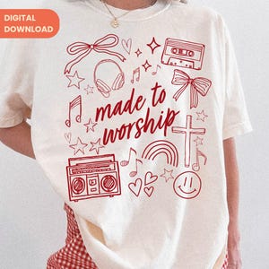 Op de afbeelding: Cr&egrave;mekleurig T-shirt met een rood grafisch ontwerp. Het ontwerp bevat een kruis, muzieknoten, een regenboog, een cassettebandje, een boombox en de woorden "made to worship". Het shirt heeft korte mouwen.