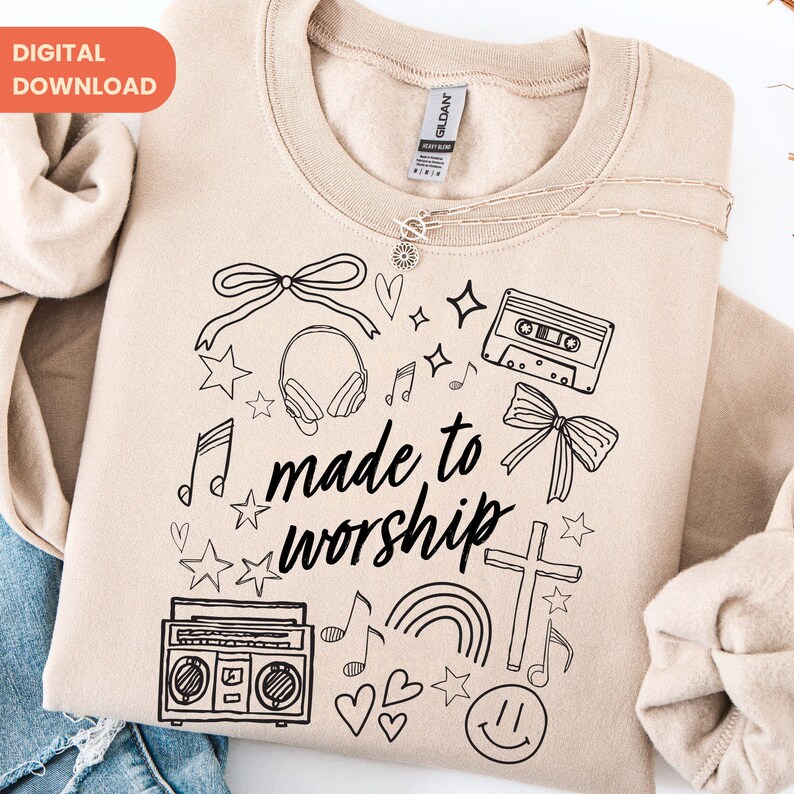 Op de afbeelding: Een beige sweatshirt met de tekst "made to worship" in een handgeschreven lettertype, omringd door zwarte lijntekeningen van muzieknoten, sterren, een cassettebandje, koptelefoon en een boombox. De woorden "DIGITAL DOWNLOAD" staan in een oranje rechthoek.
