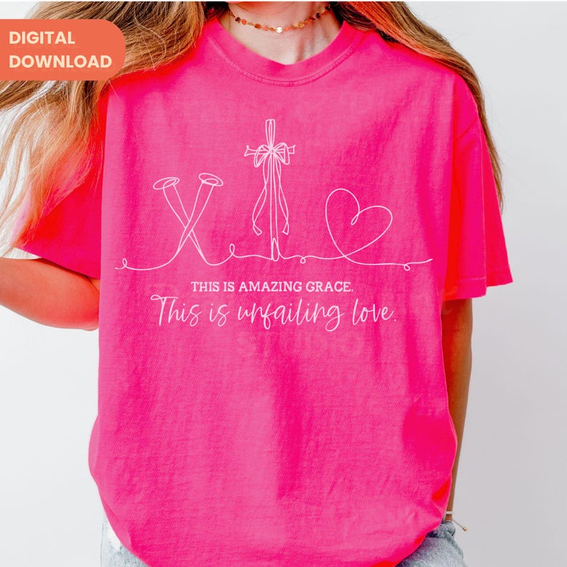 以下が含まれることがあります： 明るいピンク色のTシャツ。白い線で描かれた釘、十字架、ハートのイラストが特徴です。「THIS IS AMAZING GRACE. This is unfailing love」というテキストがイラストの下にあります。Tシャツは半袖です。