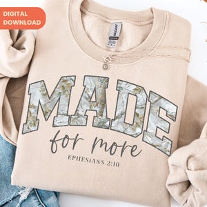 Op de afbeelding: Een beige sweatshirt met de tekst "MADE for more" in een camouflage-stijl lettertype. De tekst "Ephesians 2:10" staat eronder. Een delicate ketting met een hanger ligt op de sweatshirt. De woorden "DIGITAL DOWNLOAD" staan in de linkerbovenhoek.