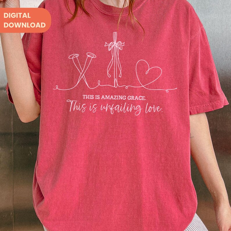 以下が含まれることがあります： 釘、十字架、ハートが描かれた白いグラフィックデザインの赤いTシャツ。「THIS IS AMAZING GRACE. This is unfailing love」の文字が下にプリントされています。シャツは半袖です。