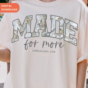 Op de afbeelding: Cr&egrave;mekleurig T-shirt met de tekst "MADE for more" in een grijze, collegiale lettertype. De letters zijn gevuld met een camouflagepatroon. De tekst "Efezi&euml;rs 2:10" staat eronder.