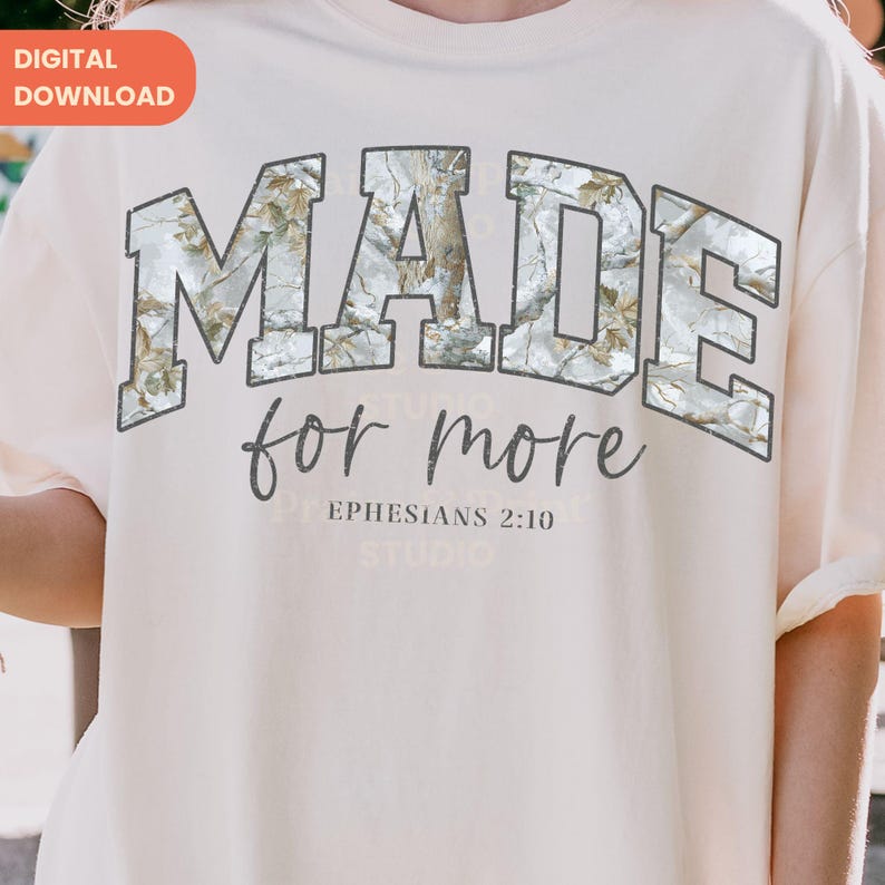Op de afbeelding: Cr&egrave;mekleurig T-shirt met de tekst "MADE for more" in een grijze, collegiale lettertype. De letters zijn gevuld met een camouflagepatroon. De tekst "Efezi&euml;rs 2:10" staat eronder.