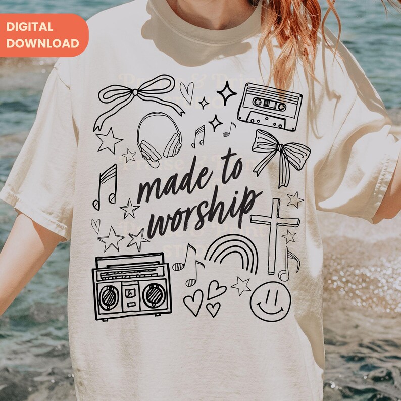 Op de afbeelding: Cr&egrave;mekleurig T-shirt met een zwart grafisch ontwerp met de tekst "made to worship", muzieknoten, sterren, een cassettebandje, een boombox, een kruis en een smiley. De woorden "DIGITALE DOWNLOAD" staan linksboven.