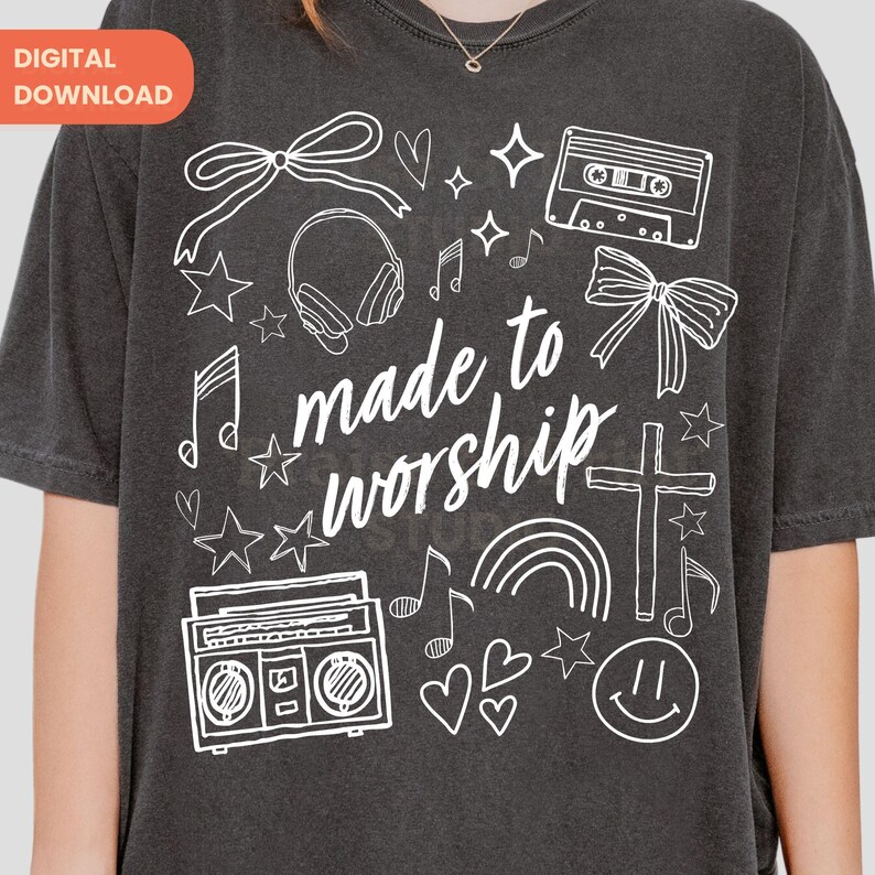 Op de afbeelding: Donkergrijs T-shirt met een wit grafisch ontwerp met een kruis, muzieknoten, sterren, harten, een cassettebandje, een boombox, een regenboog en de woorden "made to worship". Het shirt heeft een ronde hals.