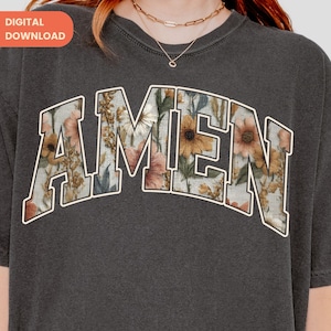 Puede incluir: Sudadera gris oscuro con cuello redondo y la palabra "AMEN" en un diseño floral en el pecho. Las letras están delineadas en blanco, y el estampado floral incluye flores rosas, amarillas y verdes. La sudadera tiene un aspecto vintage.