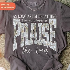 Può includere: T-shirt grigio scuro con la scritta "AS LONG AS I'M BREATHING I've got a reason to PRAISE the Lord." La parola "PRAISE" ha un motivo mimetico. Un'etichetta di download digitale si trova nell'angolo in alto a sinistra.