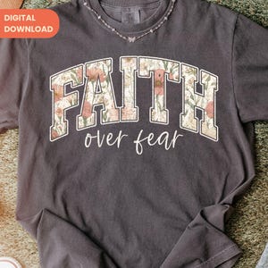 May include: Dark gray t-shirt with the words "FAITH over fear" in a floral design. The text is in a collegiate style font. The shirt has a crew neck and short sleeves. A digital download tag is in the upper left corner.