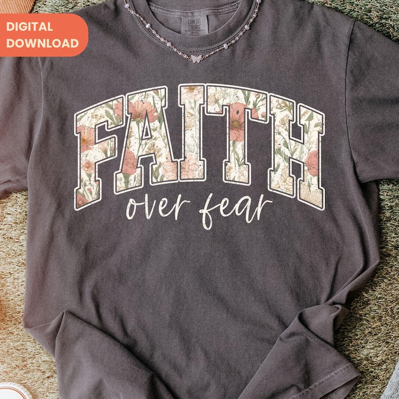 May include: Dark gray t-shirt with the words "FAITH over fear" in a floral design. The text is in a collegiate style font. The shirt has a crew neck and short sleeves. A digital download tag is in the upper left corner.