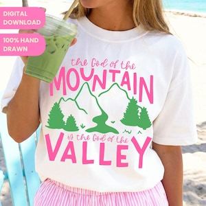 May include: White t-shirt with the text "the God of the MOUNTAIN is the God of the VALLEY" in pink and green. The design includes mountain and tree graphics. The words "DIGITAL DOWNLOAD" and "100% HAND DRAWN" are in a pink box.