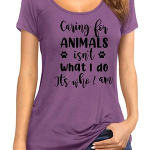 May include: Purple short-sleeved t-shirt with the text "Caring for ANIMALS isn't what I do It's who I am" and two paw prints.