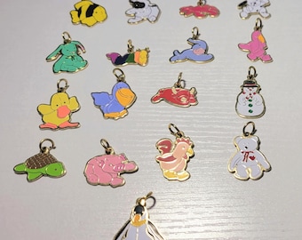 May include: A collection of metal charms featuring various animals, a snowman, and a penguin, alongside a set of small plush bear and animal figures, each with a small attached tag featuring a red heart logo and printed text.